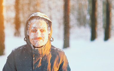 Fototapeta na wymiar Fun portrait of an young frozen man. Jogging in a blizzard in the woods. Face covered with snow and frost. Closeup portrait of happy young guy smiles in cold weather in the winter forest at sunset.
