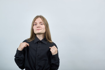 Attractive caucasian young woman in fashion black shirt isolated on gray background in studio pulls shirt with fingers, looking at camera. People sincere emotions, lifestyle concept.