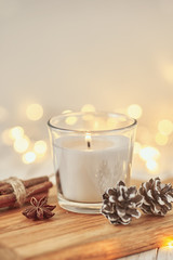 White burning candle with decorations and garland lights in bokeh on a wooden table. Cozy home and hygge concept