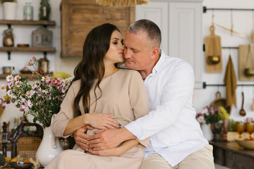 First pregnancy.  Concept-a happy man hugs his pregnant wife's stomach while sitting in the kitchen. The wife kisses the future father.