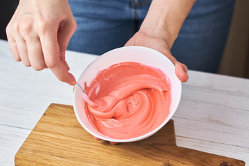 Woman whisking red cream for decorating cookies in a bowl on kitchen, closeup