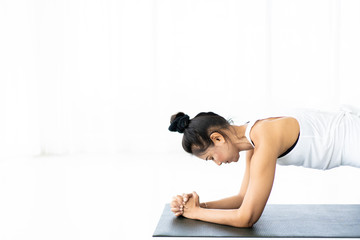 Strong Asian woman doing an exercise in the room near window with natural lighting, woman planking on the ground, photograph with copy space. Beautiful Asian woman portrait.