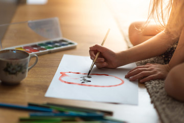 A child paints with a brush and paints on a wooden floor on a white sheet on a sunny day