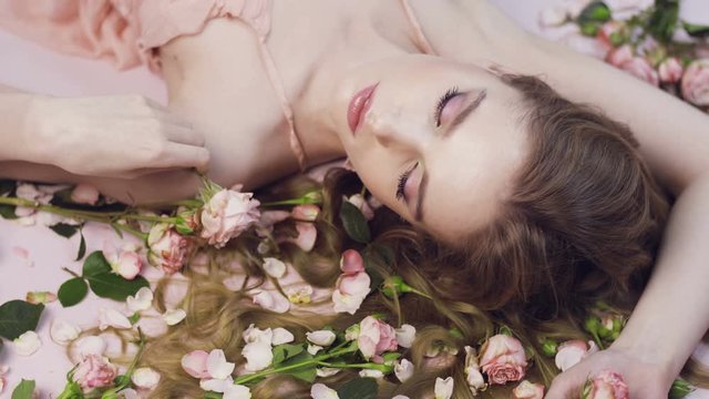 Beautiful girl lies in roses. Delicate scarlet roses and a woman. Aromatherapy Valentine's Day. Natural cosmetic. Gentle perfume.