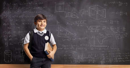 Schoolboy with books and backpack standing in front of a blackboard