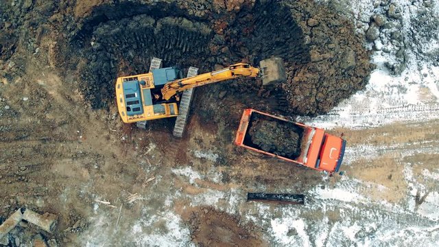Modern construction machines work at a career with sand, stones. Aerial view from above of a construction site with excavator and truck working.