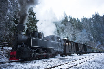 Old or vintage Train Billowing Smoke in the Snow as it Moves Through the forest Mountains