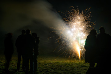 Friends stand together as silhouettes around a firework fountain to celebrate the new year at...