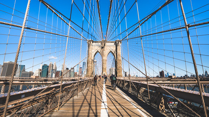 Unidentified people walk and ride bicycle on Brooklyn bridge in New York City, sunny day. United states tourism landmark, American city life, USA tourist attraction, or commuter transportation concept