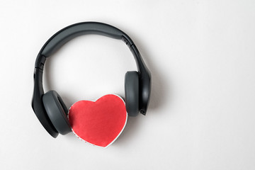 Fototapeta na wymiar Full-size wireless headphones pulled over small red heart-shaped box on white table. Love music concept. Directly above