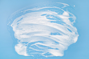 White soapy foam on a blue background. Cleaning/Washing concept..