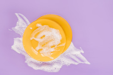 Yellow plates with white soapy foam on a purple background. Washing dishes concept. Flat lay, Top view.