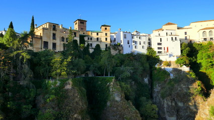 Fototapeta na wymiar viele Häuser reihen sich am Felsrand von Ronda entland des steilen Abhangs unter blauem Himmel