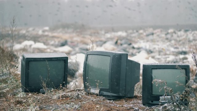 Switched-off TVs with a grabage site in the background