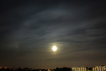 Bright circular ice halo around the moon with parhelium to the left. Beautiful optical phenomena in the night sky.