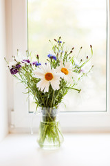 Bouquet of chamomiles and cornflowers in   vase on   table.
