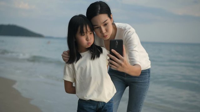 Holiday concept. Mother and daughter are taking pictures with mobile phones on the beach. 4k Resolution.