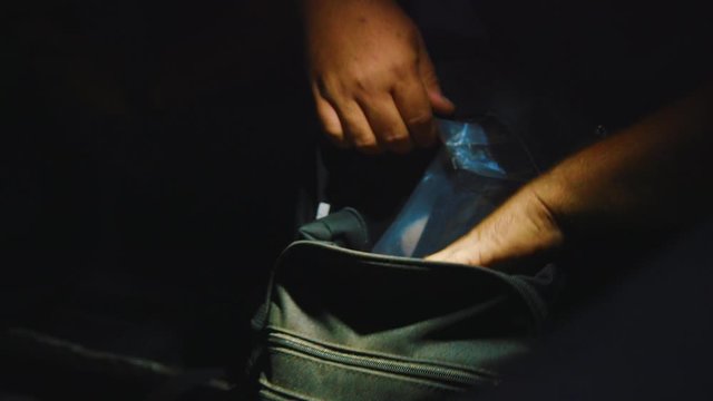 A young man looking inside his backpack and a flashlight helping him see - Close up
