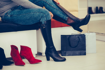 Woman  trying on new pair of winter boots with high heels while sitting at a fashion store