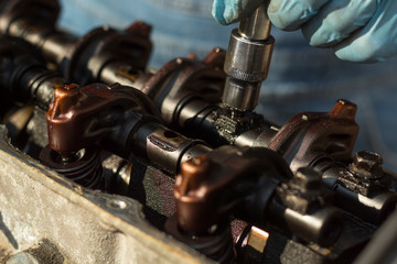 Dłoń mechanika odkręca śrubę w silniku za pomocą klucza nasadowego. Odkręcanie popychaczy zaworów i wałka. Wnętrze starego silnika.