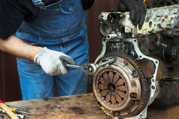 Mechanik samochodowy w rękawicach roboczych odkręca sprzęgło od bloku silnika podczas naprawy w warsztacie. - obrazy, fototapety, plakaty