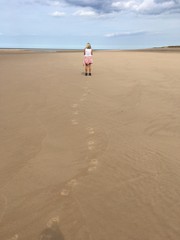 Foot prints of woman walking on beach from behind