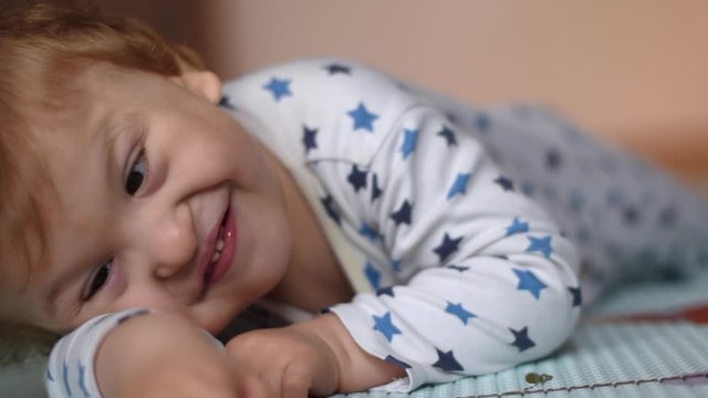 Portrait of a happy baby with cerebral palsy lying on his belly and playing at home. Special needs child. Handicapped baby boy close-up.