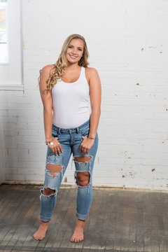 Sexy young blonde woman poses in studio wearing white tank top and ripped blue jeans