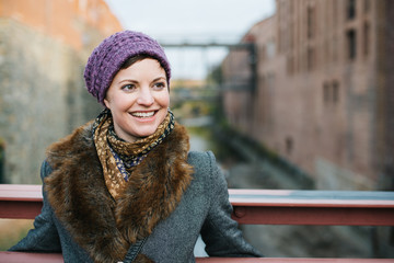 Smiling Caucasian woman portrait smiling and looking away, head and shoulders dressed in warm clothing wearing a knit hat and standing on a bridge over the canal in Georgetown, Washington DC.  - 312826614