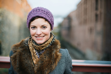 Smiling Caucasian woman portrait smiling and looking at the camera head and shoulders dressed in warm clothing wearing a knit hat and standing on a bridge over the canal in Georgetown, Washington DC.  - 312826659