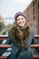 Smiling Caucasian woman portrait smiling and looking away, head and shoulders dressed in warm clothing wearing a knit hat and standing on a bridge over the canal in Georgetown, Washington DC.  - 312826696