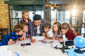 Curious pupils watching attentively their Korean male teacher use device of tablet computer to...