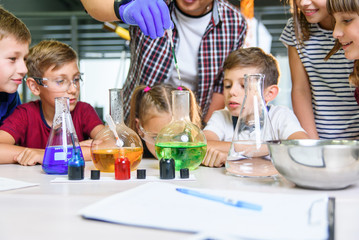 Test tubes with colorful liquid substances. Study of liquid states. Group school pupils with test tubes study chemical liquids. Science concept. Girls and boy providing experiment with liquids.