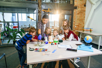 Schoolchildren with young male teacher on lesson of chemistry doing an interesting experiments...