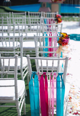 The decor is the venue of the wedding ceremony, wooden white chairs decorated with ribbons of bruise, pink flowers and different colors.