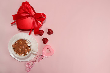 Greeting card for Valentine's Day or Women's Day with a cup of cocoa with marshmallows. Red hearts and gift box on a pink background, top view. Holiday greetings, modern woman concept