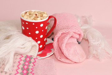 Modern woman's table with a cup of cocoa, a scarf, socks, pink background, the concept of winter comfort and the Hygge style, warm clothes and a hot drink in cold weather