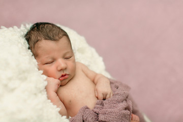 Sleeping newborn baby girl laying on a cream colored blanket on a pink purple backdrop with a headband in her hair