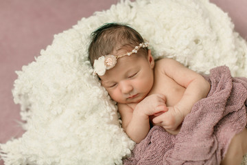 Sleeping newborn baby girl laying on a cream colored blanket on a pink purple backdrop with a headband in her hair