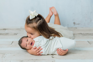 3 year old big sister kissing her newborn little sister in a cool tone white room
