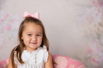 Obraz na płótnie Canvas cute little preschool age girl in a white dress in a pink floral room sitting on a chair