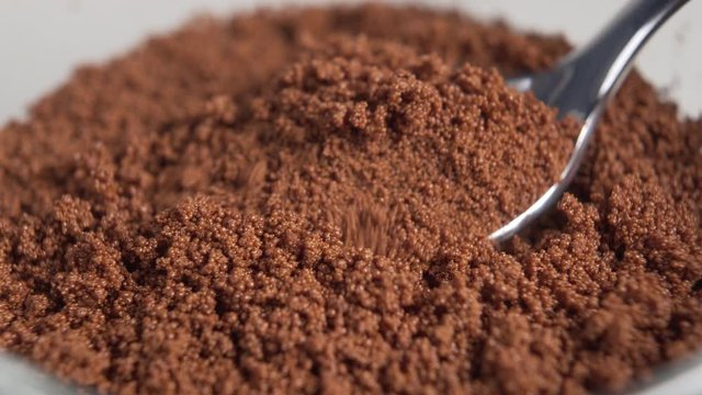A hand with a shiny dessert spoon scoops instant chicory powder from a glass cup close-up. Rotation. Macro video