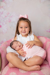 3 year old big sister holding her newborn little sister and smiling