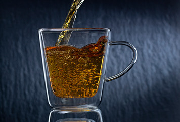 Tea is poured into a glass cup, on a dark background
