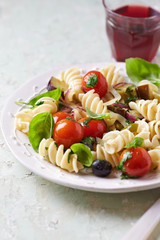 Big fusilli pasta with cherry tomatoes, zucchini, black olives and fresh basil on bright wooden background. 