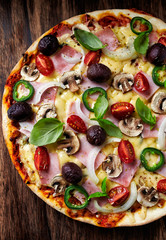 Pizza with ham, cheese, cherry tomatoes, jalapeno pepper, kalamata olives and champignon mushrooms. Dark wooden background. Top view.