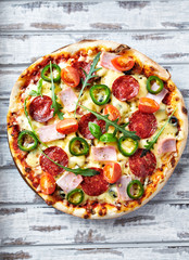  Pizza with ham, salami, jalapeno pepper, cherry tomatoes, cheese and rocket. White wooden background. Top view.