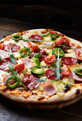 Pizza with ham, salami, jalapeno pepper, cherry tomatoes, cheese and rocket. Rustic wooden background. T