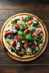 Pizza with cherry tomatoes, spinach, red onion and fresh basil. Rustic wooden background. Top view.