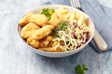 Chicken nuggets with raw salad and french fries on bright wooden background.